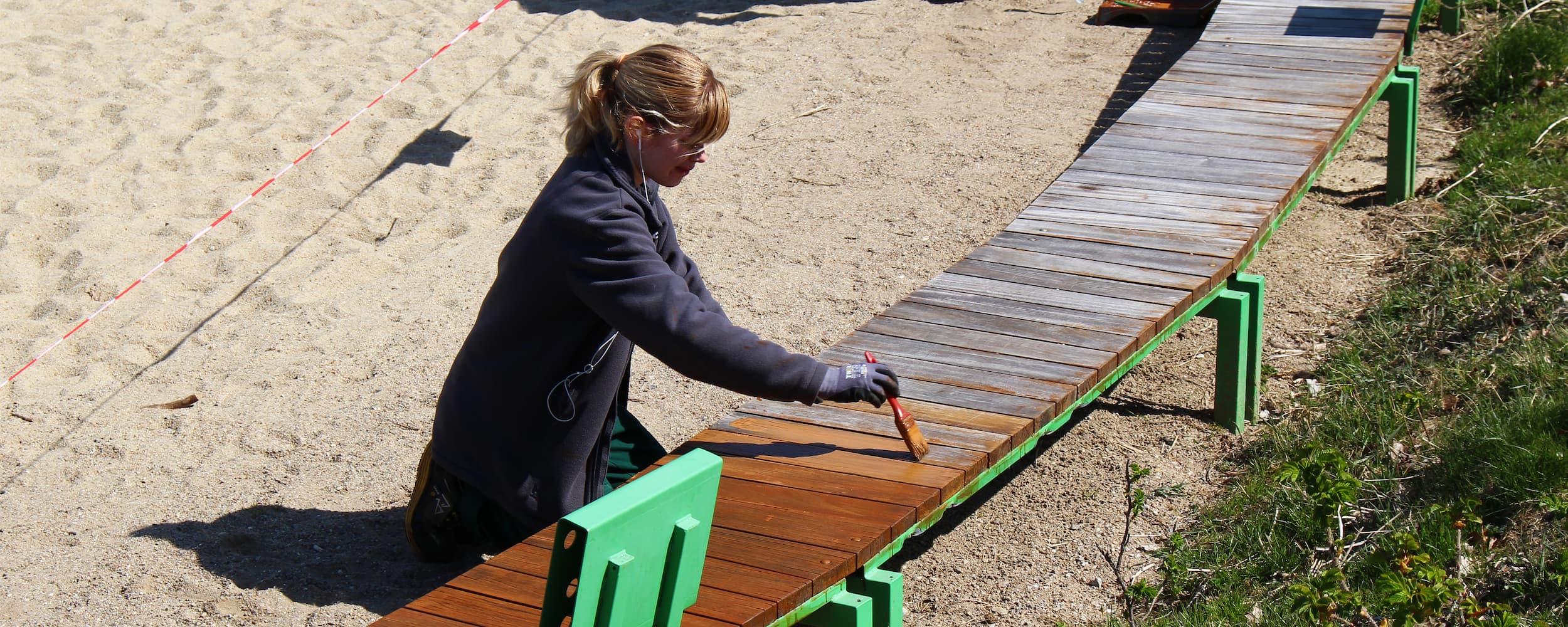Ørestads drift maler en bænk med et træbeskyttende middel.