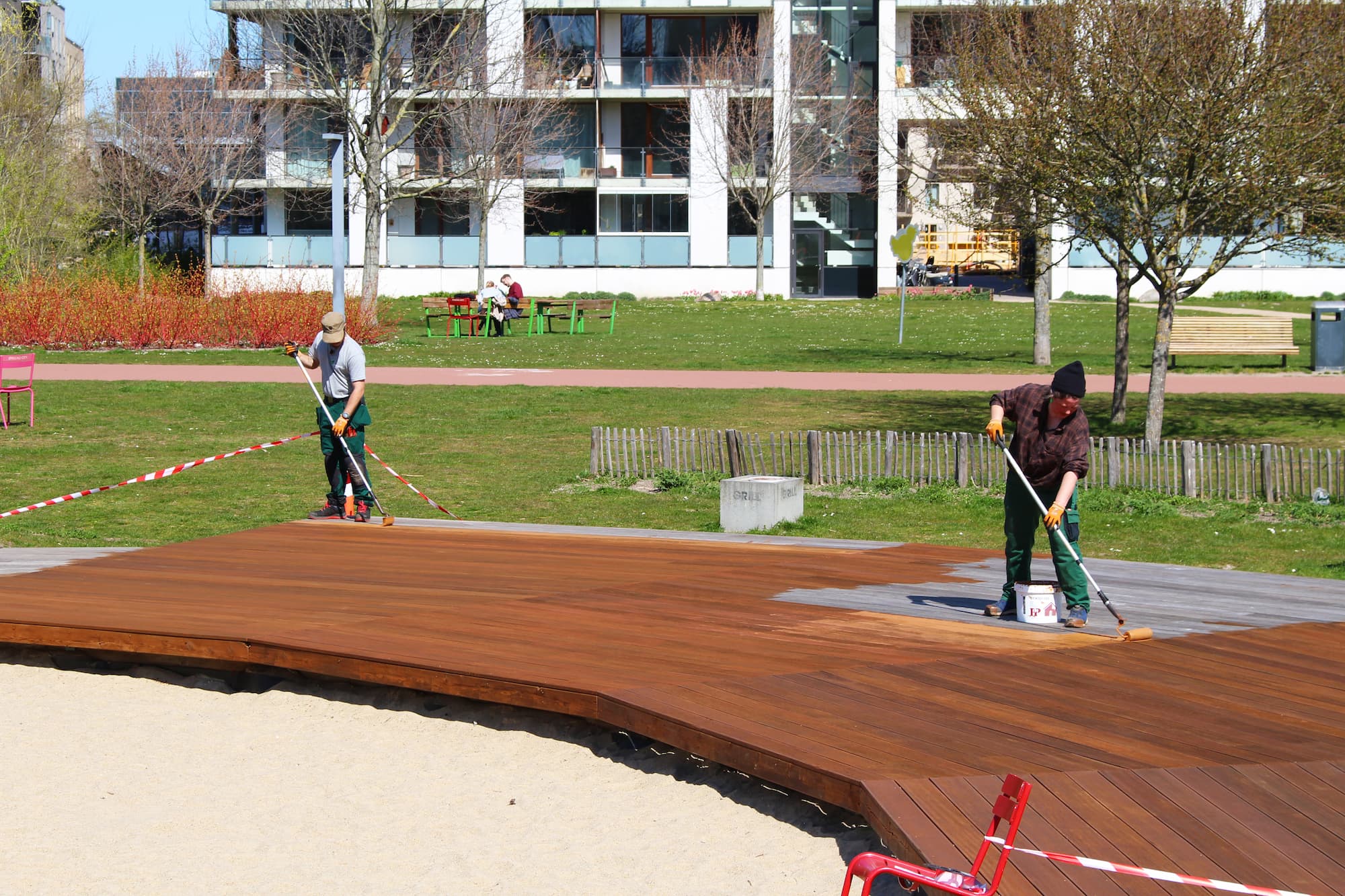 Ørestads driftsfolk maler træplatformen med beachvolleybanen i Byparken med et træbeskyttende middel.