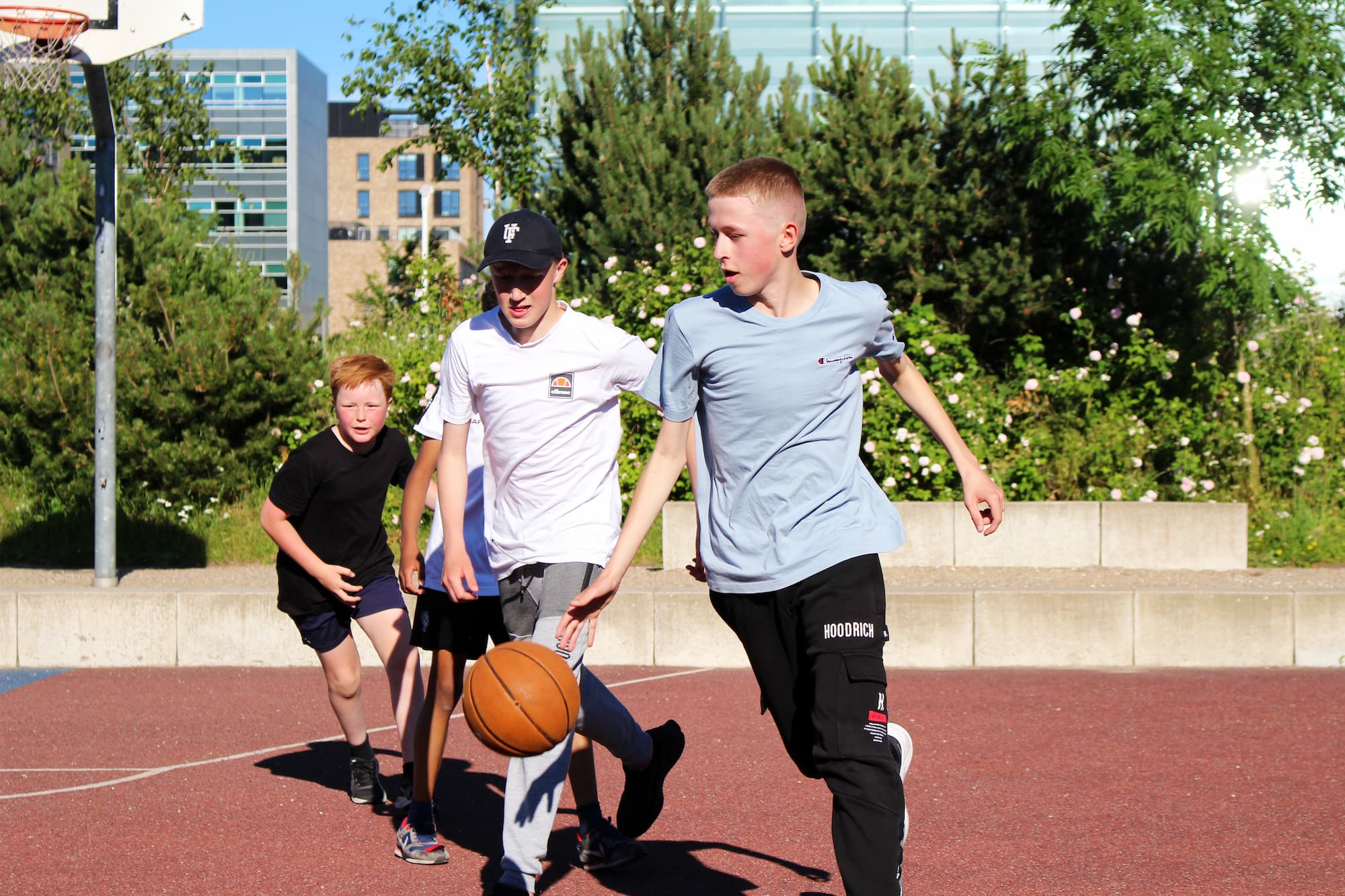 En gruppe unge spiller basketball på parkens multibane.