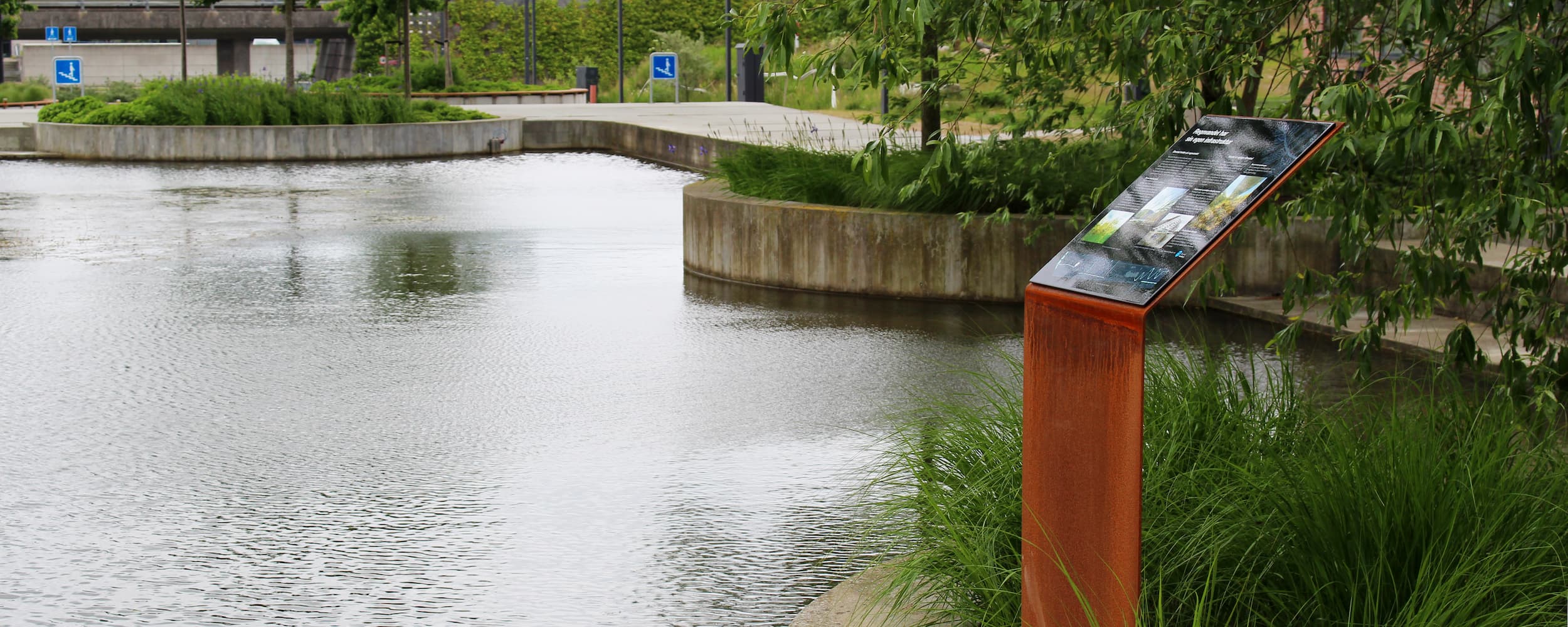 Ørestad Vandlaug har i samarbejde med grundejerforeningerne opsat nye skilte i byrummet, som formidler viden og fakta om bydelens kanaler og søer. På billedet ses et af de blå skilte på "Kanalpladsen" i Arenakvarteret.