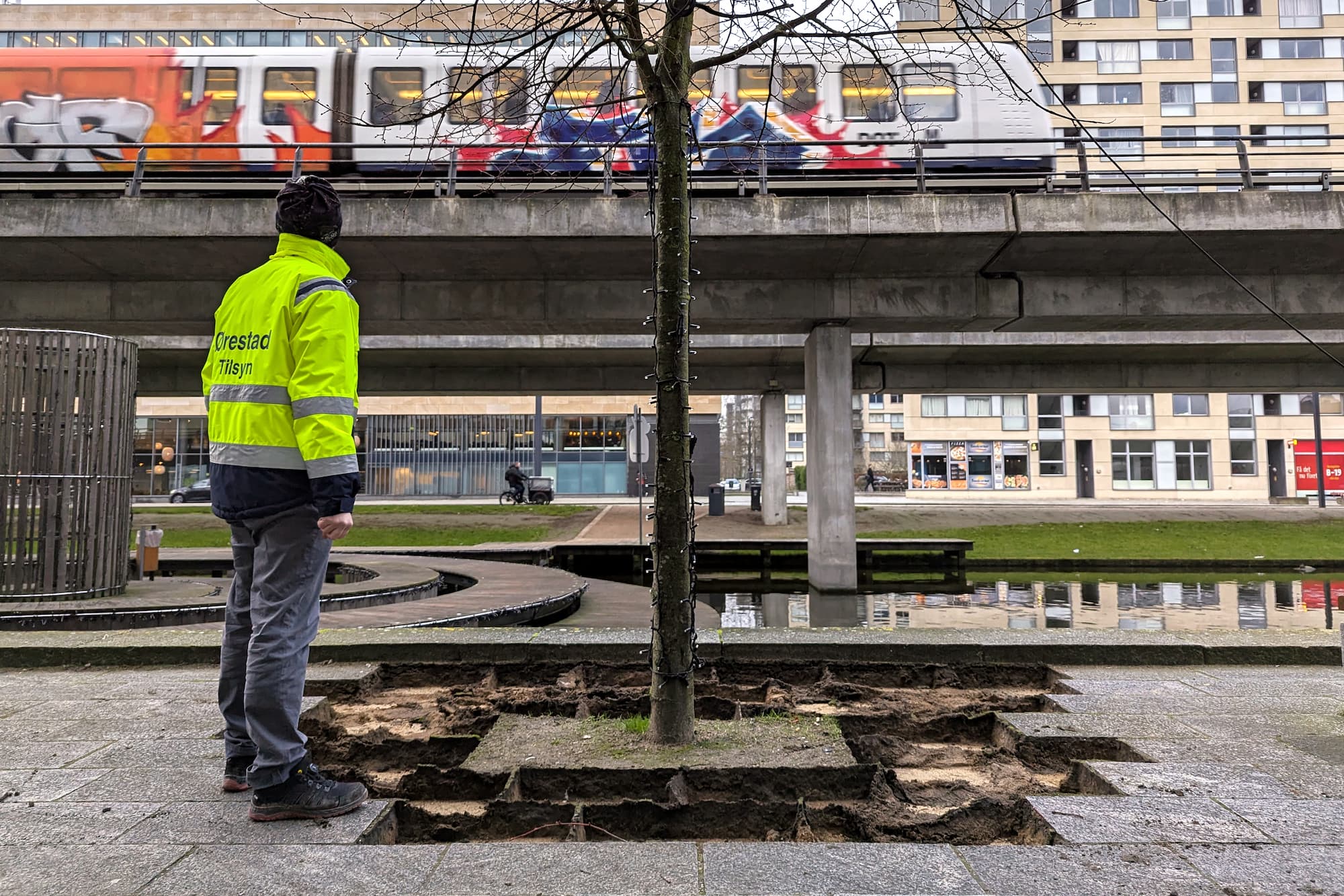 Der er fjernet fliser i Sivegaden for at gøre plads til blosmterbede. I baggrunden suser metroen forbi.