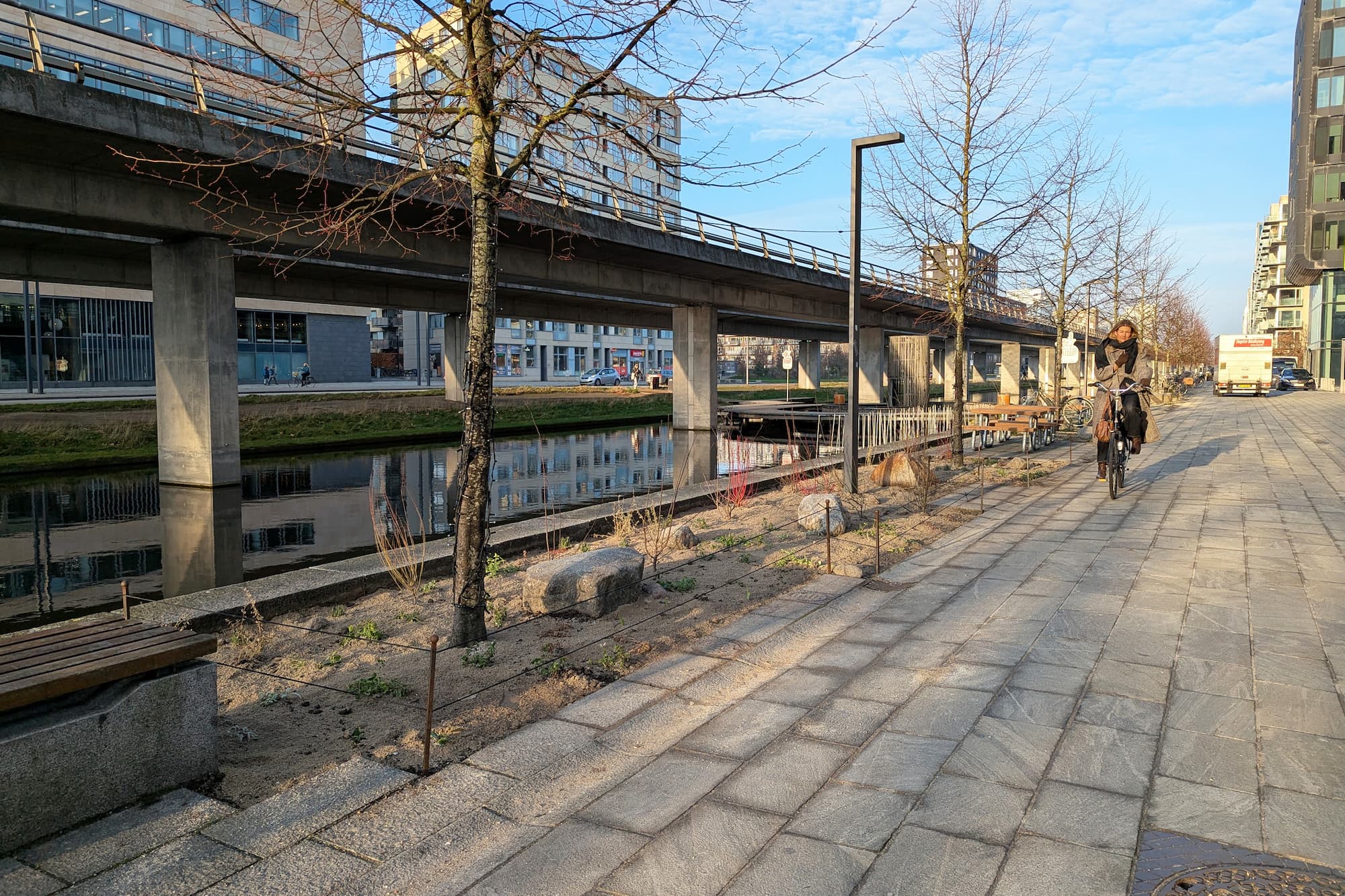 Langs kanalen ved Ørestad Bibliotek og Gymnasium er nogle fliser fjernet for at gøre plads til blomsterbede, mens nye bænke, stole og plantekummer indbyder til ophold.